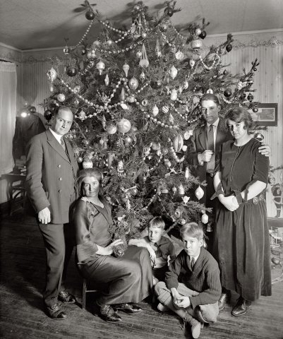 Three generations of a family gather around the Christmas tree wearing their funeral faces.